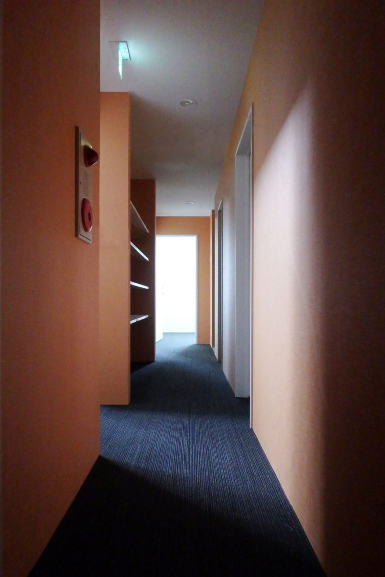 2階中廊下。オレンジの壁とブルーの床の組み合わせ。