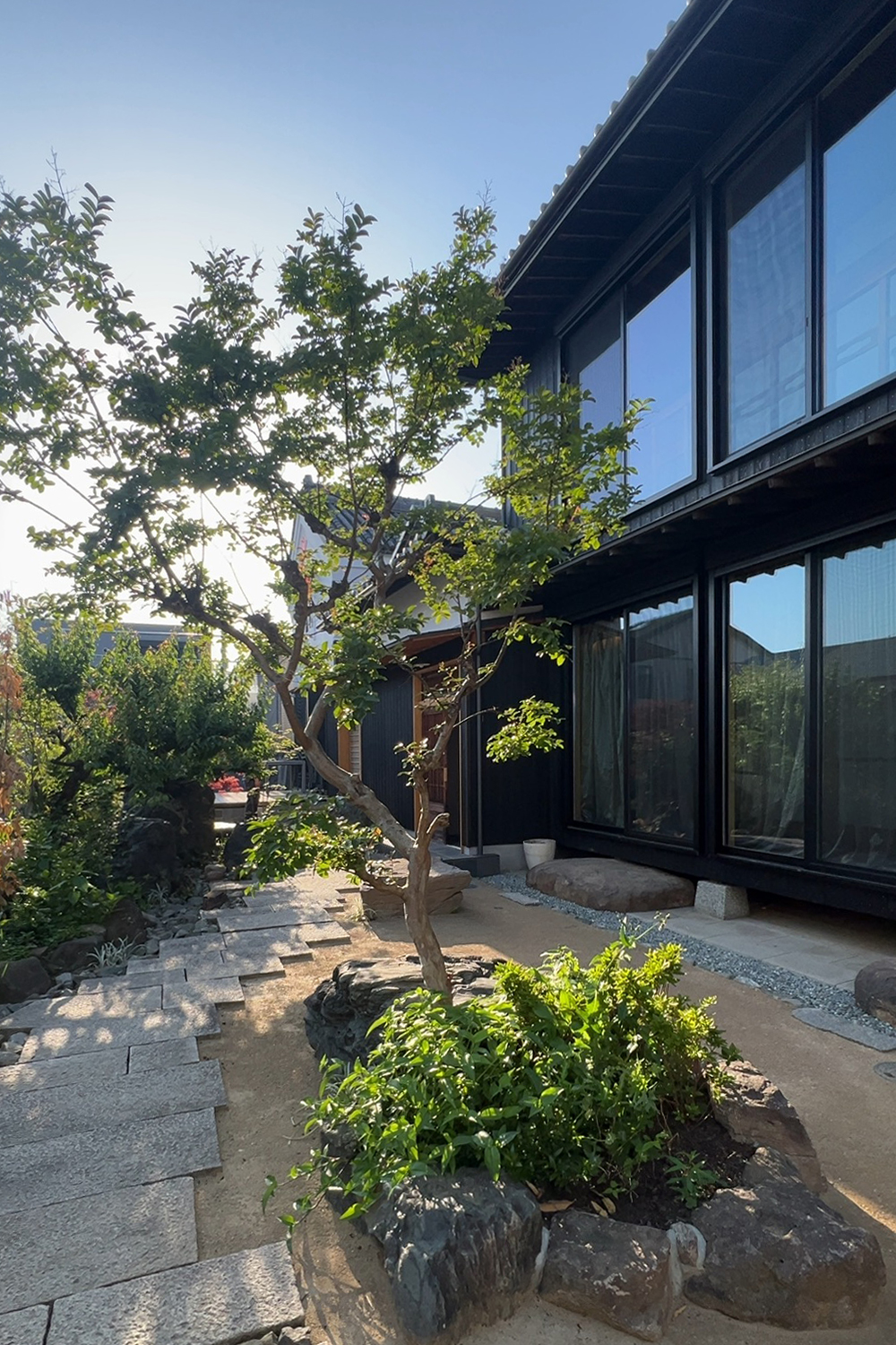 古いアルミサッシを高断熱サッシに全交換、外壁は焼杉と漆喰。アプローチは増築された小屋を除去し、既存の庭石を再利用して組み直し。