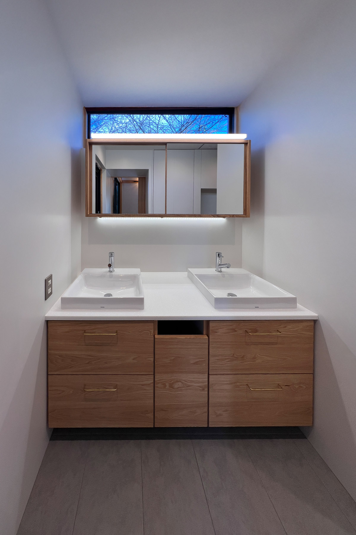 2ボウルの洗面室。対面するマンションからプライバシーを守りつつ、高窓から桜の老木を望む。フロアキャビネットは中央にダストボックスを格納。足元はロボット掃除機のドックを兼ねて少し浮かせている。