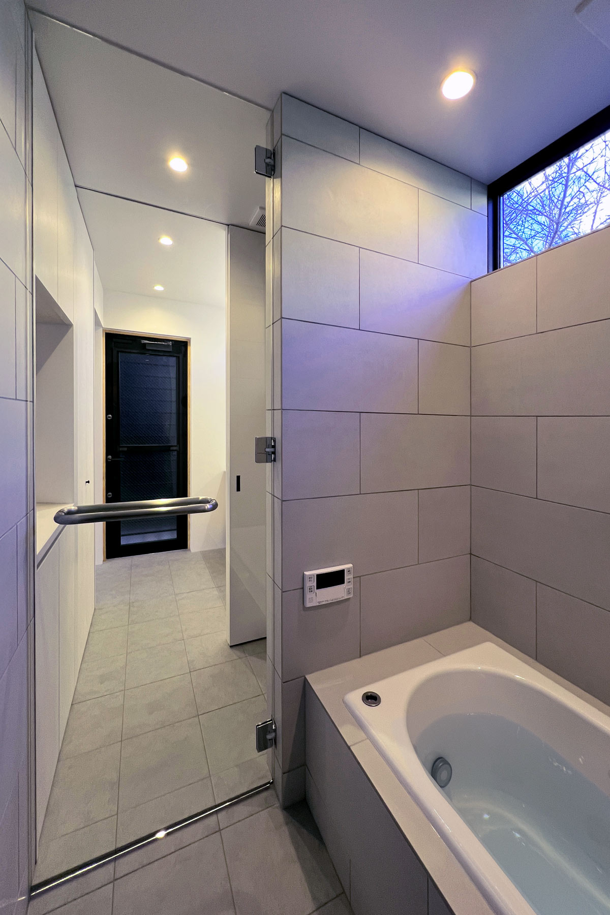 洗面からランドリーを介して浴室へつながるバスルーム。来客時は引戸を閉じてプライバシーを守る。外遊びの汚れを落とせるようにウッドデッキ直結として床はサーモタイル貼り。